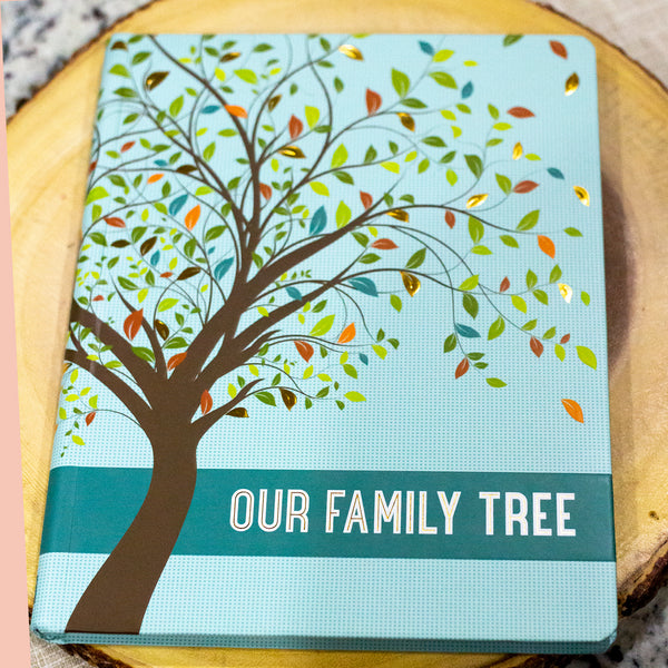 Our Family Tree Book: A graceful tree adorns the cover, with leaves in shades of spring green, olive, teal, orange, brick red, and gold foil. The words 'Our Family Tree' appear in white letters traced with gold foil. Smooth matte hardcover with a subtle blue/green check pattern. Raised embossing lends texture and dimension. Rounded corners for reduced wear.